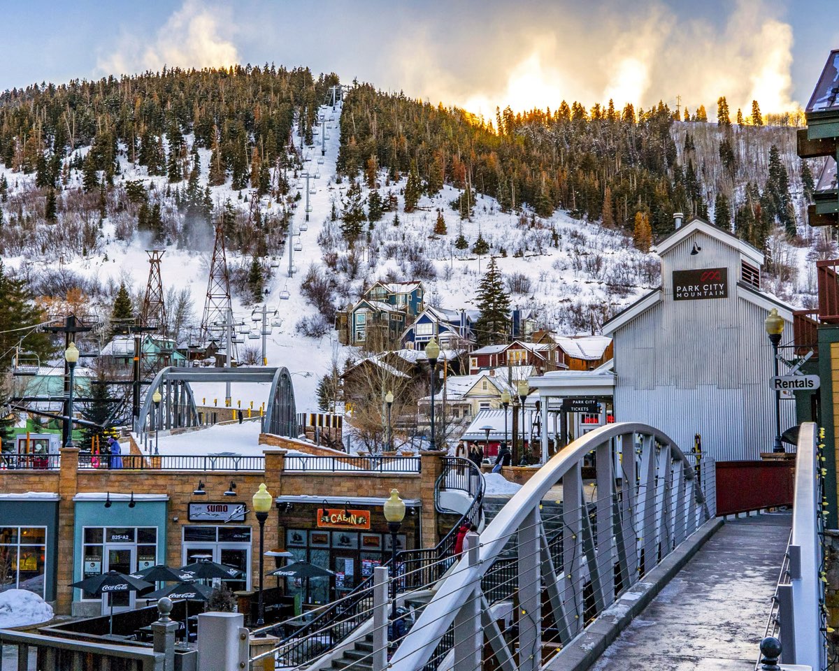 Park City Mountain's Town Lift climbing the snowy slope above shops and a pedestrian bridge off Main Street in Park City, Utah